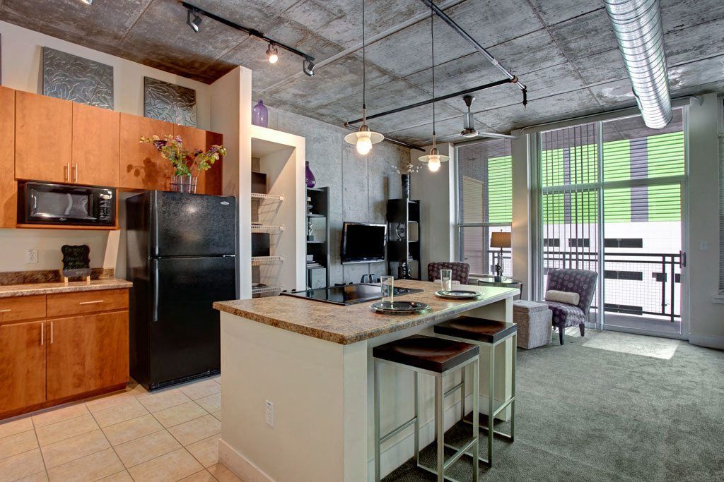 Modern kitchen here at Skyline Lofts Apartments with wood cabinets, granite countertops, and stainless steel appliances. A dining table set with plates and green glass bottles adds elegance.