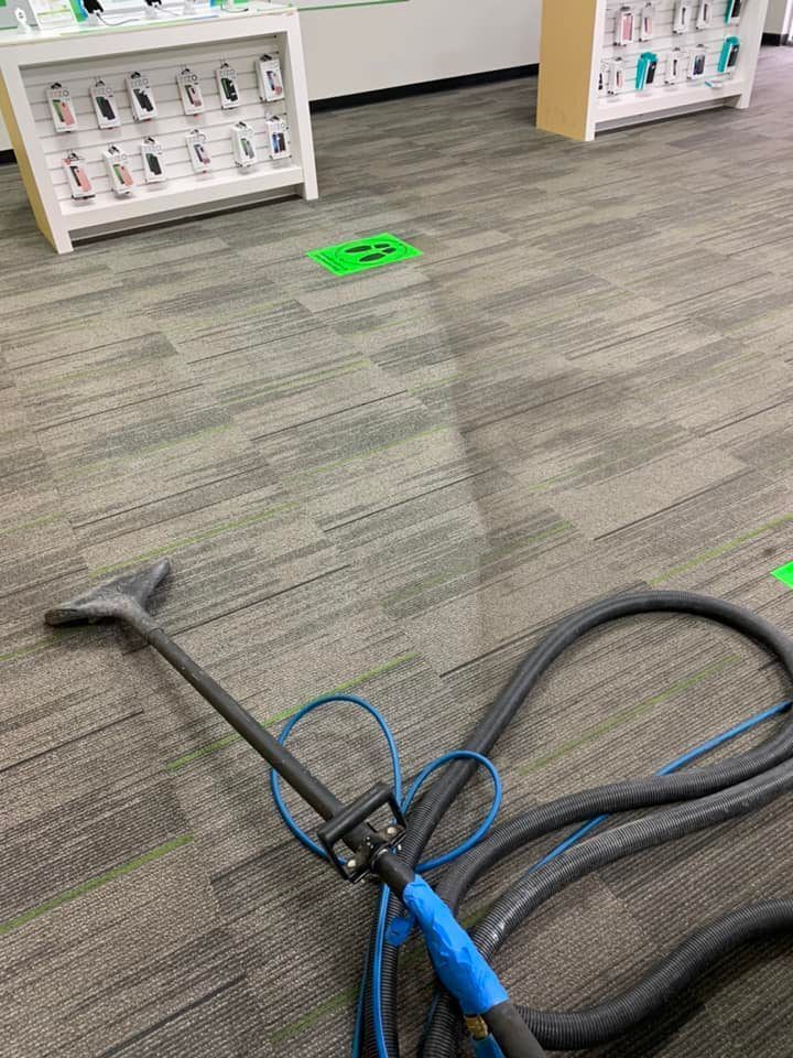 Carpet being cleaned in a store with gray carpet, cleaning tool in foreground, display cases in background.