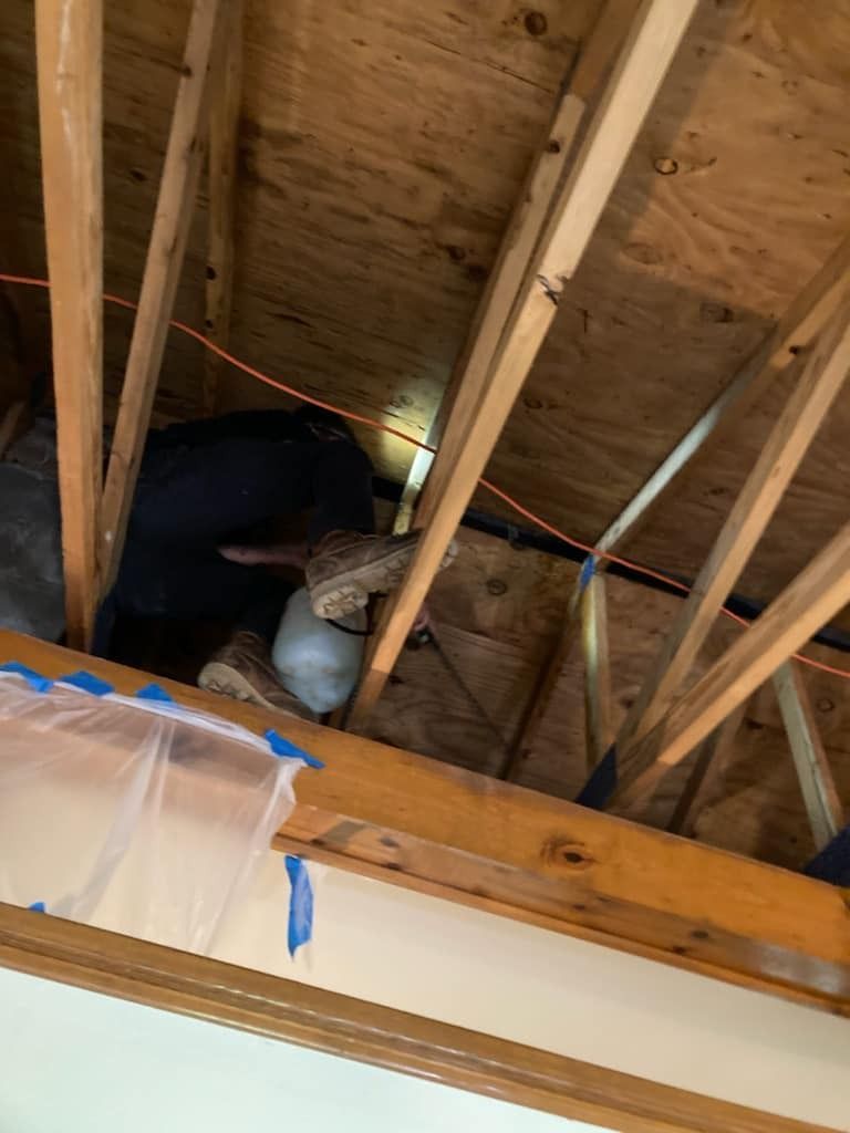 Inside a home's attic: A person in dark clothing looks at a bundle of insulation and other materials near the rafters.