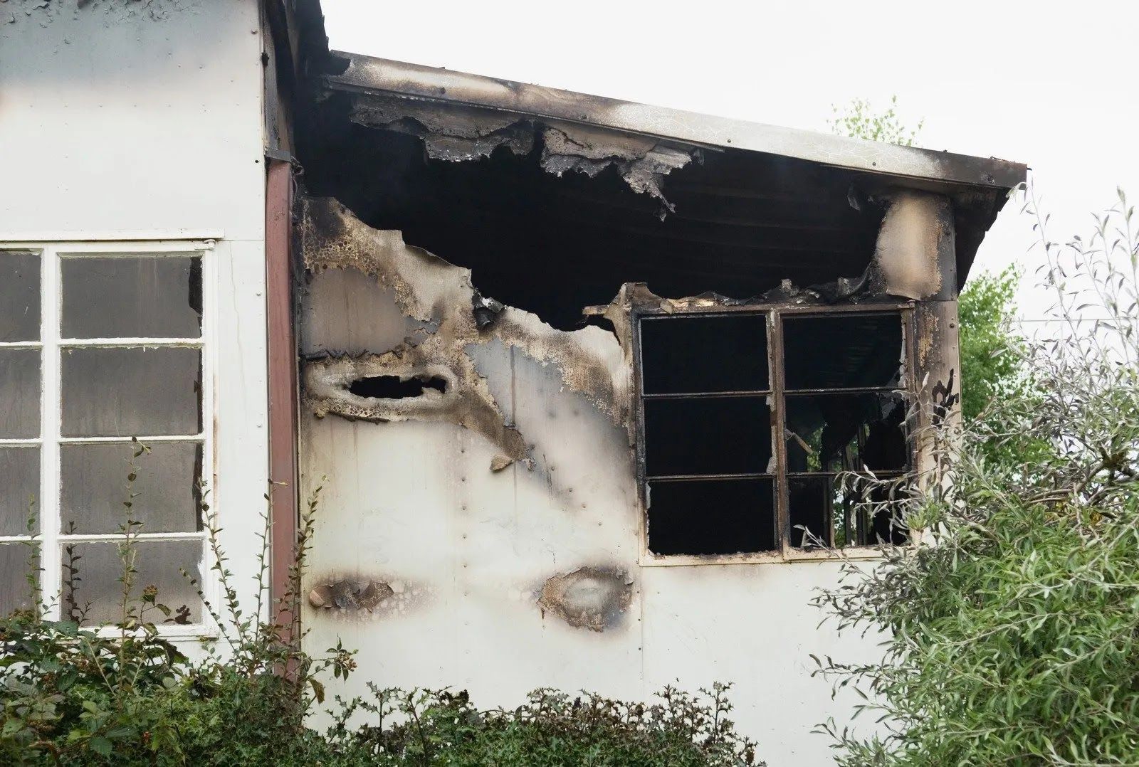 Exterior of a building with significant fire damage around a window, showing charred wood and blackened surfaces.