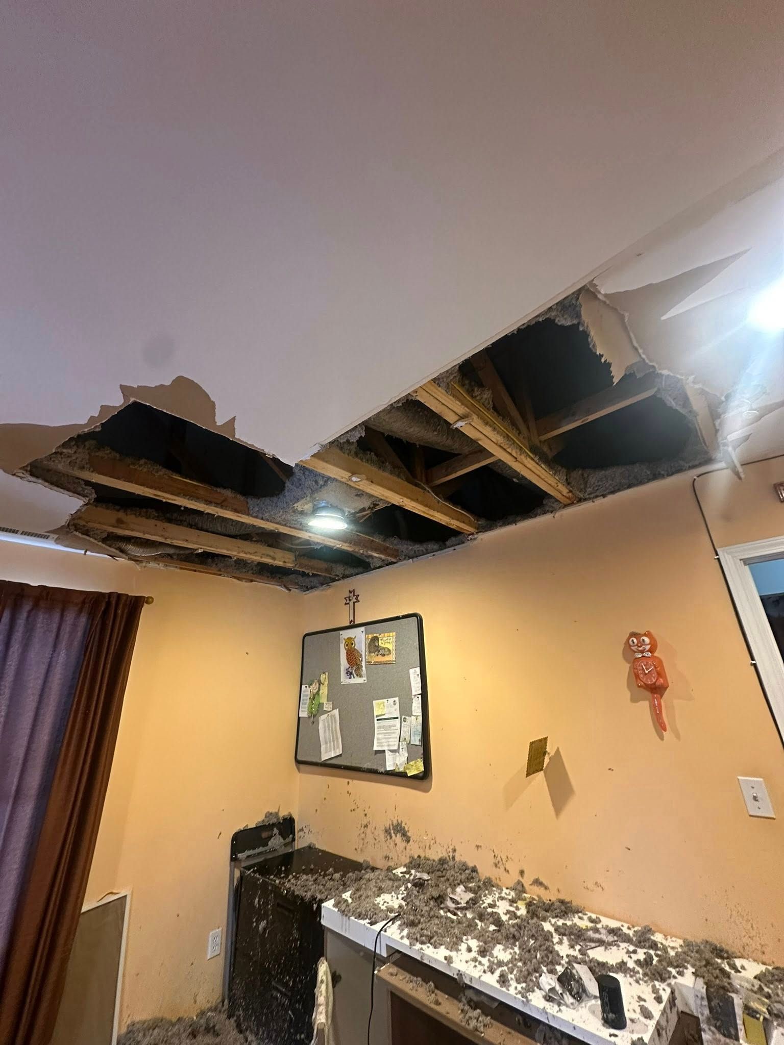 Damaged ceiling with large holes exposing wooden beams. Debris covers counters and floor.