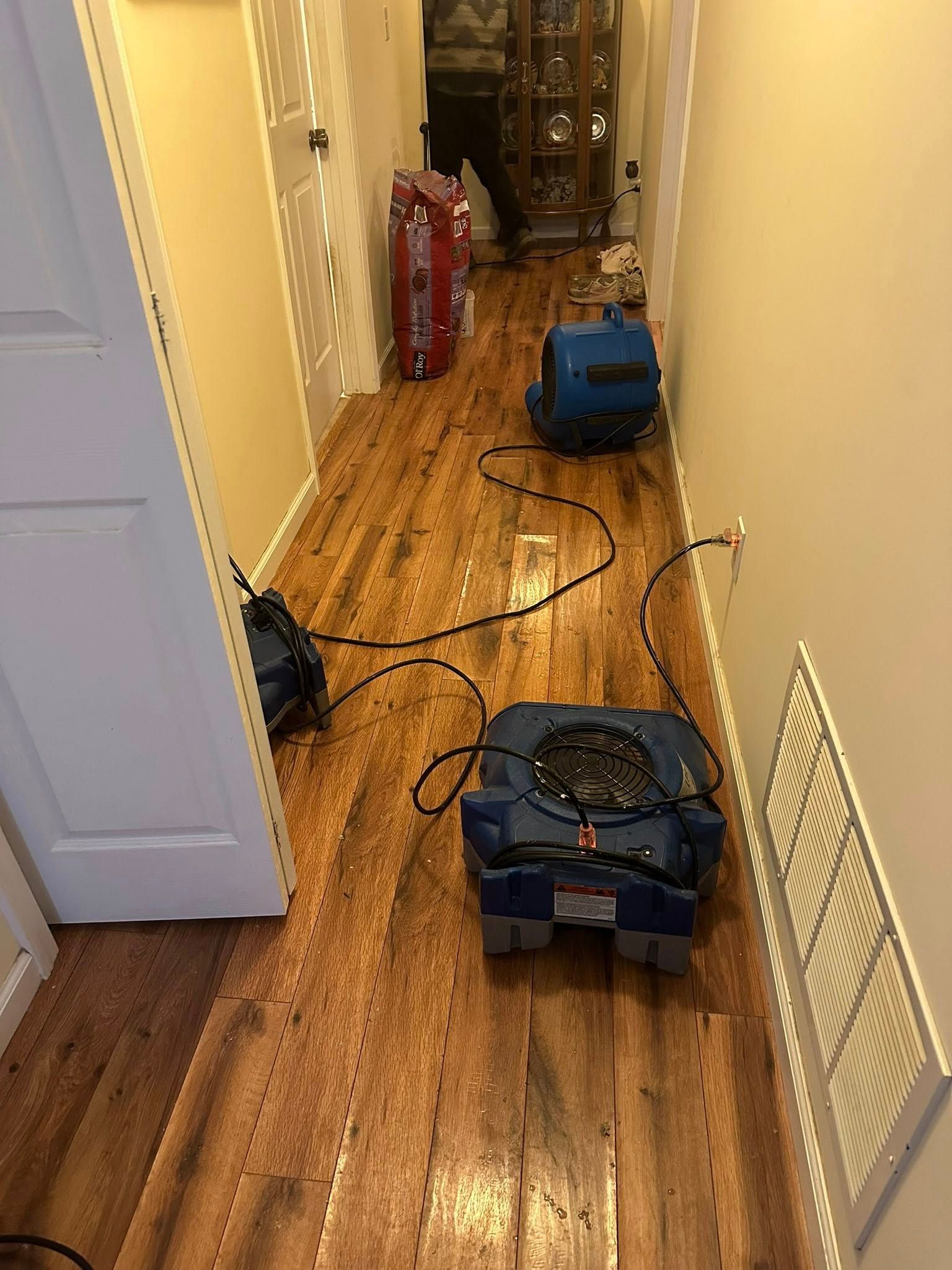Three blue air movers and one red case on wet wooden floor in a hallway.