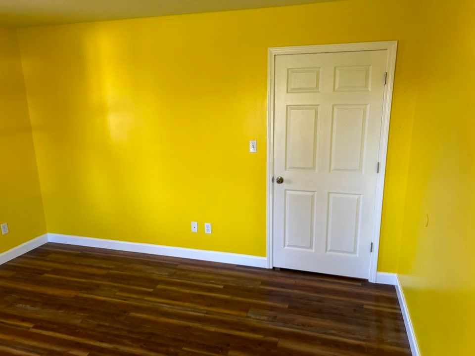 Yellow-painted room with a white door and wood-look flooring.