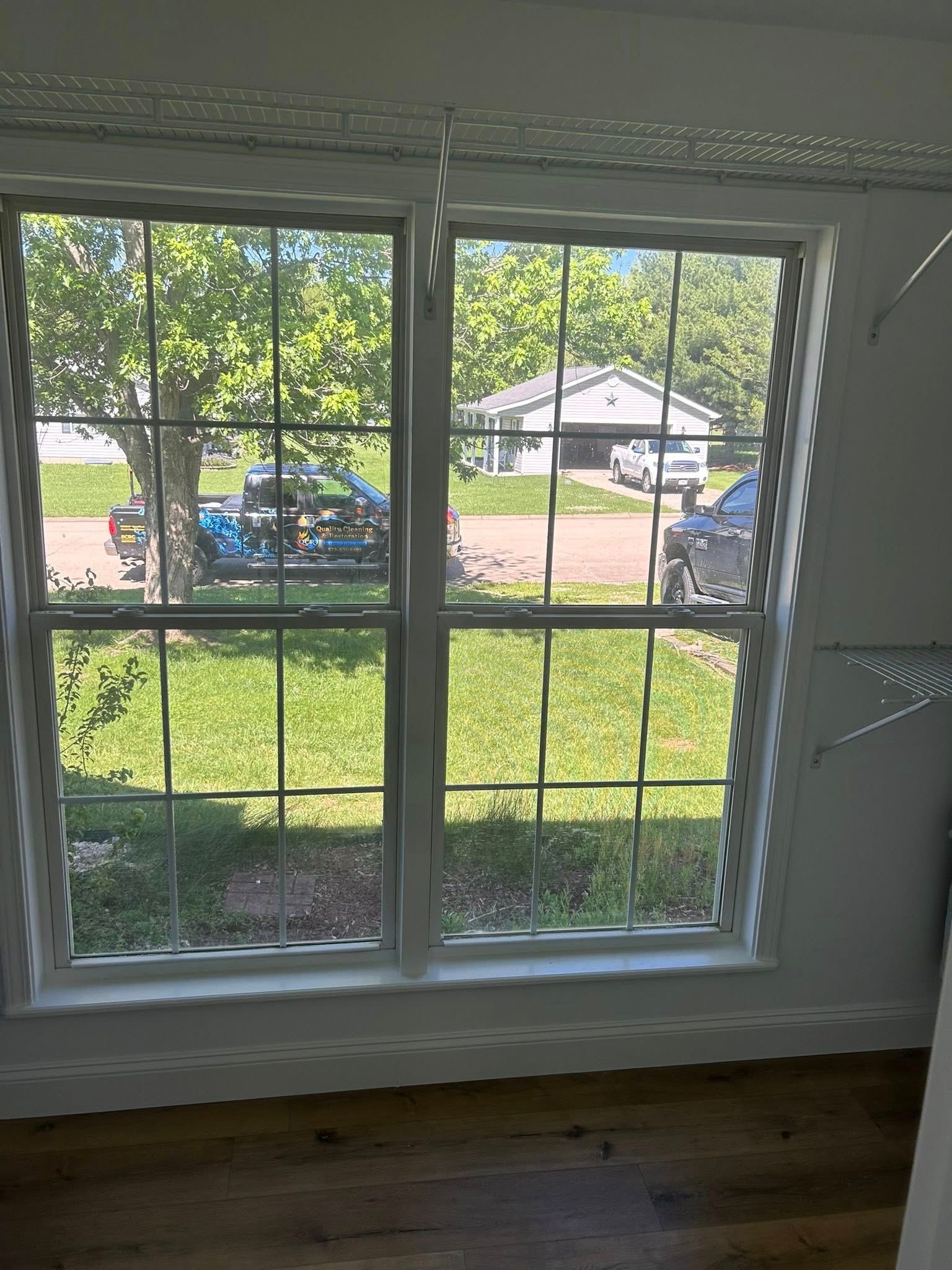 Two white-framed windows with grid patterns overlook a neighborhood street. A truck and car are visible outside.