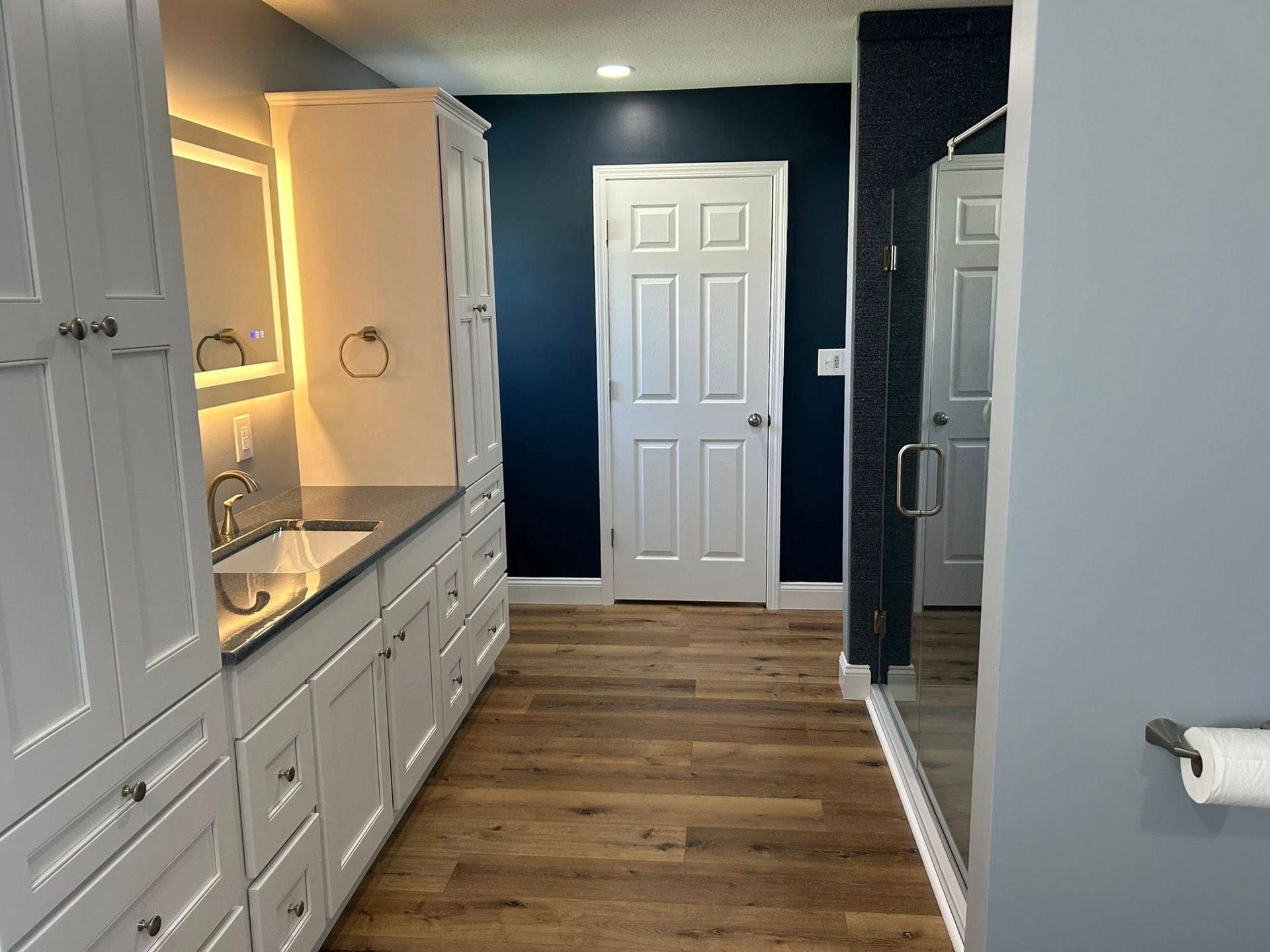 Bathroom with white cabinets, silver hardware, navy blue walls, and a glass shower door.