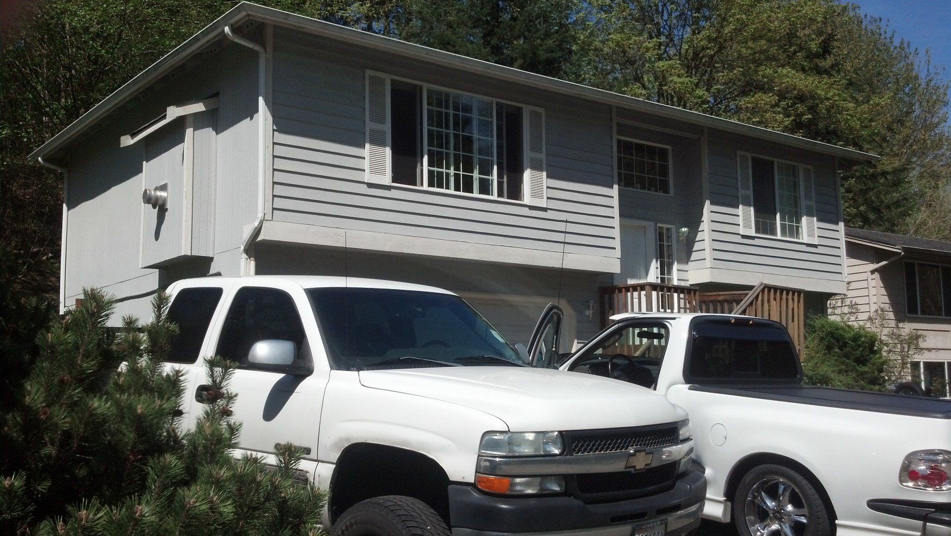Two white trucks are parked in front of a house
