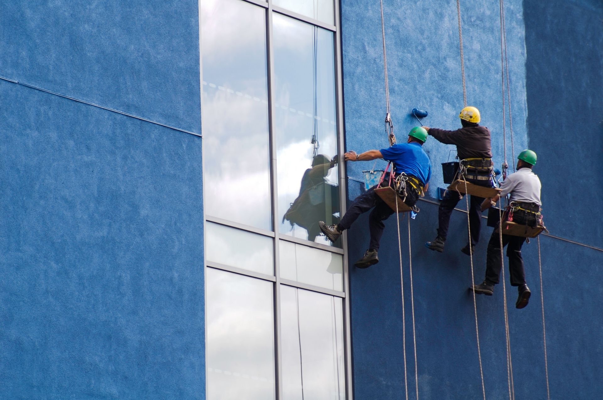 Three men are cleaning the windows of a blue building.