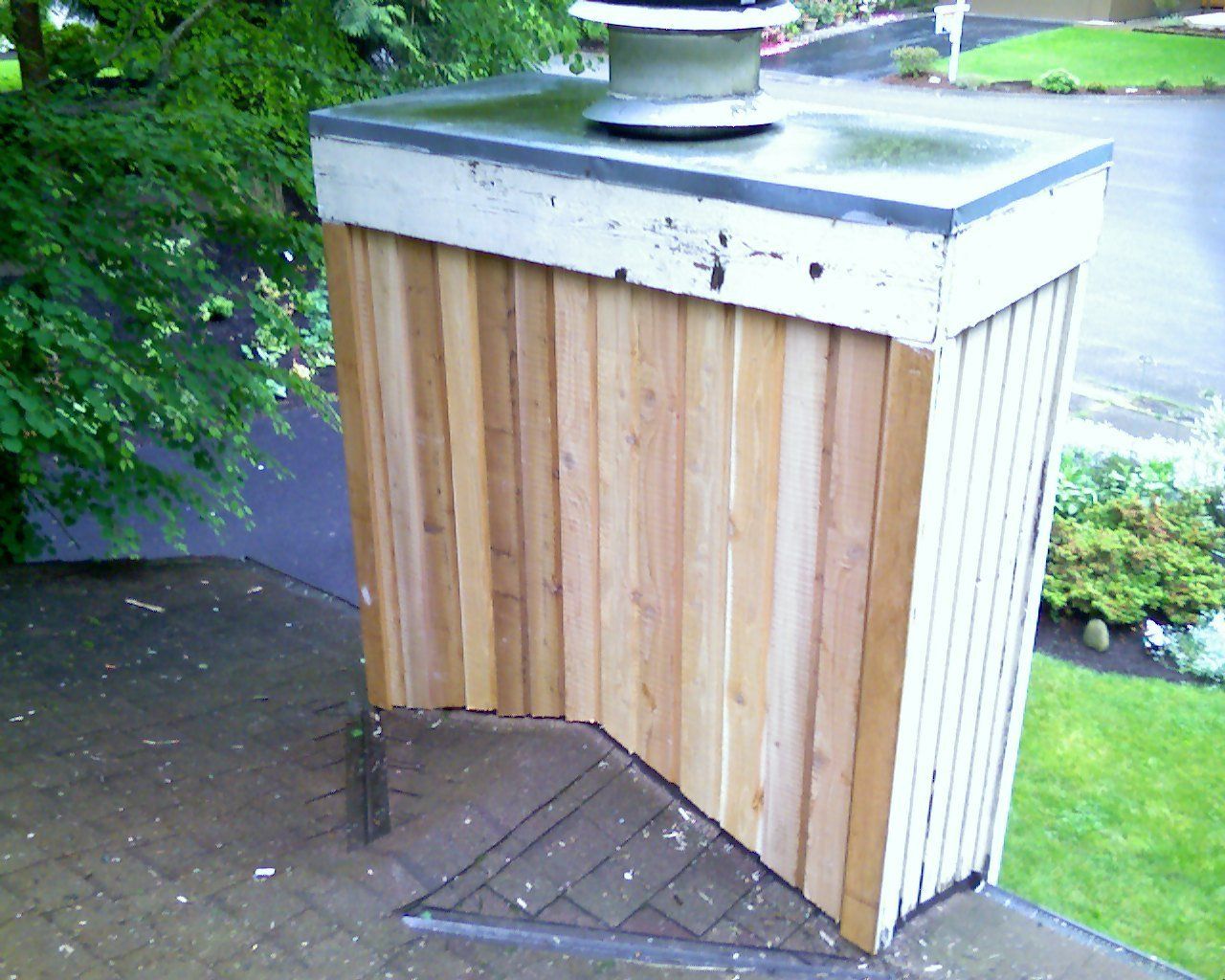 A wooden chimney with a metal top sits on a brick patio