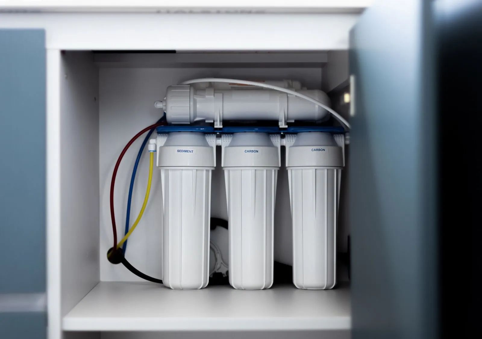 Under-sink water filtration system with three white filter cartridges and color-coded tubing