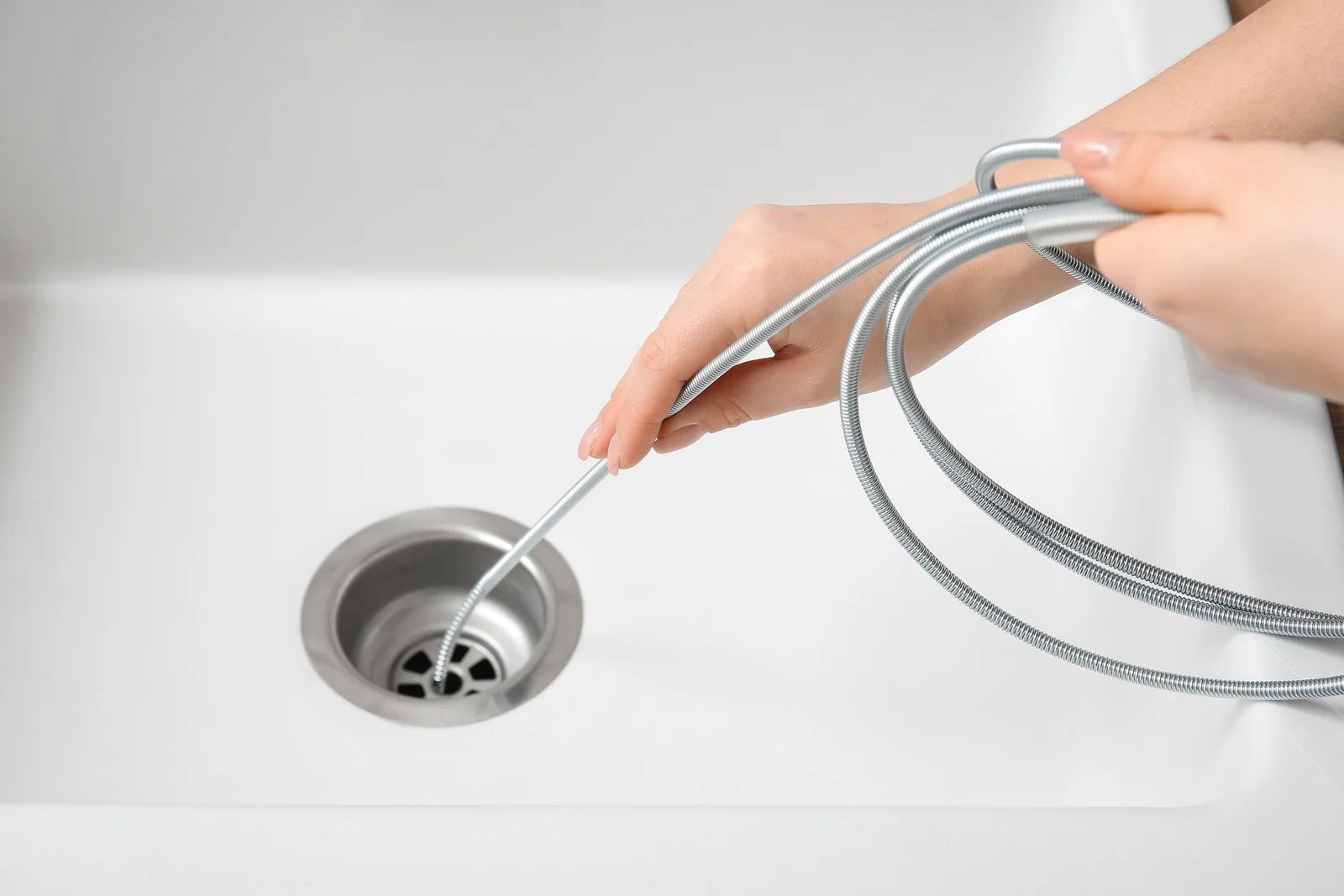 Hand using a drain cleaning tool to clear a sink drain