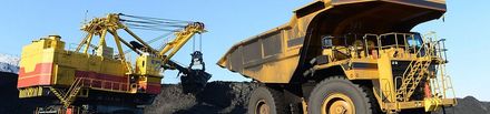 A large yellow dump truck is being loaded with coal by a crane.