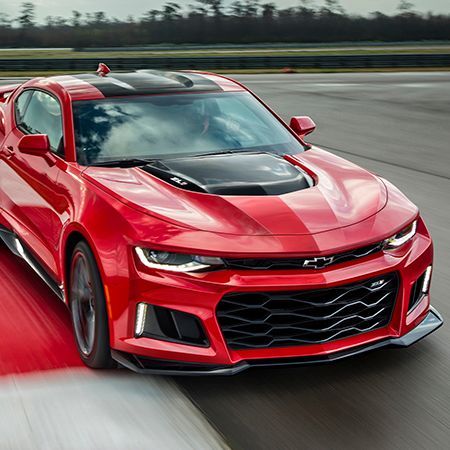 A red chevrolet camaro is driving down a road.