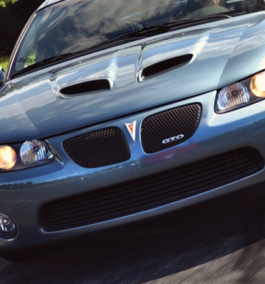 A blue gto car is driving down a road