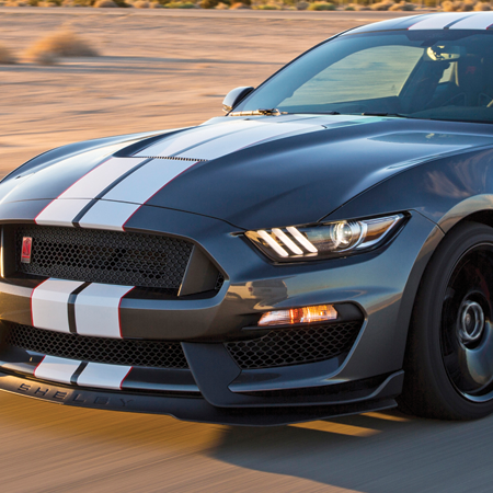 A black mustang with white stripes is driving down a road