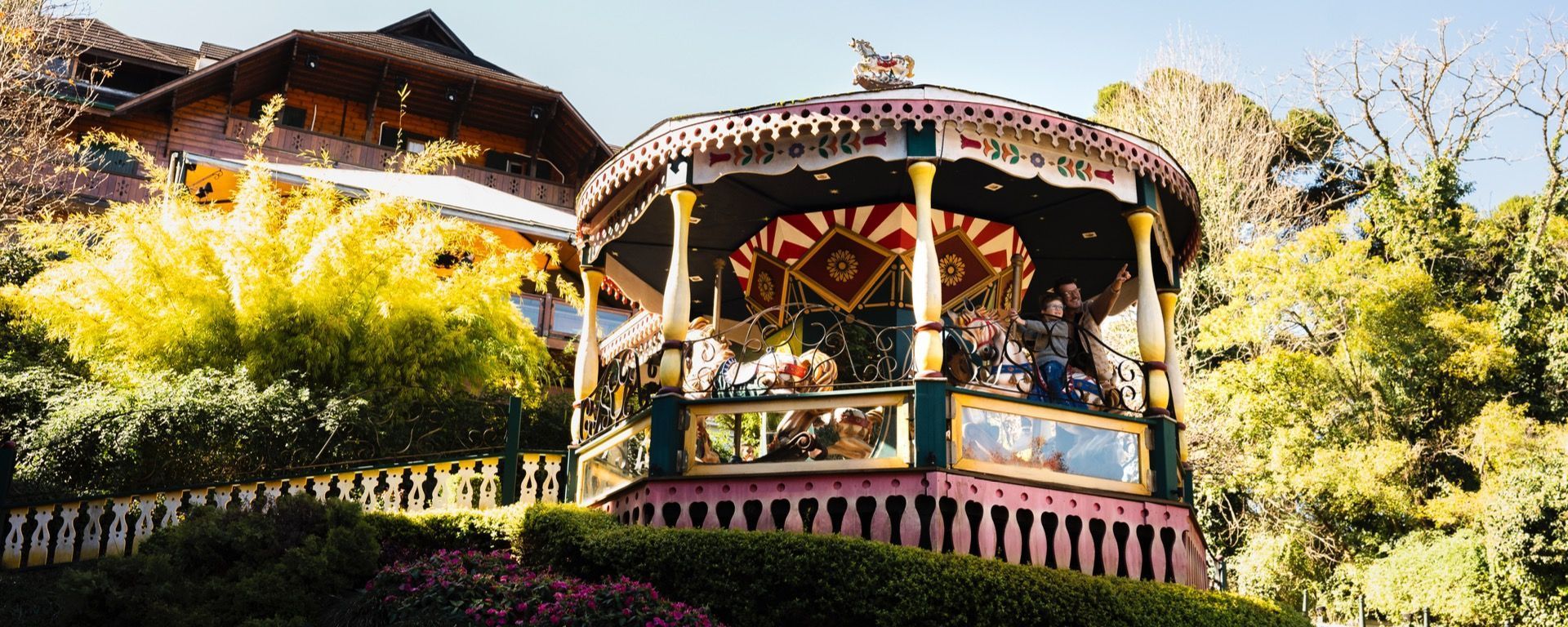 Gazebo decorado ao ar livre com pessoas, rodeado por bambus e flores verdejantes em um jardim ensolarado.