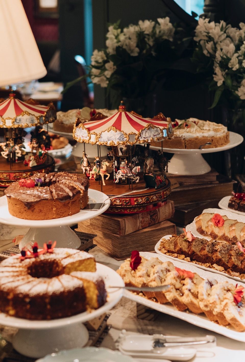 Uma variedade de bolos e doces em uma mesa de sobremesas com um carrossel decorativo como peça central.