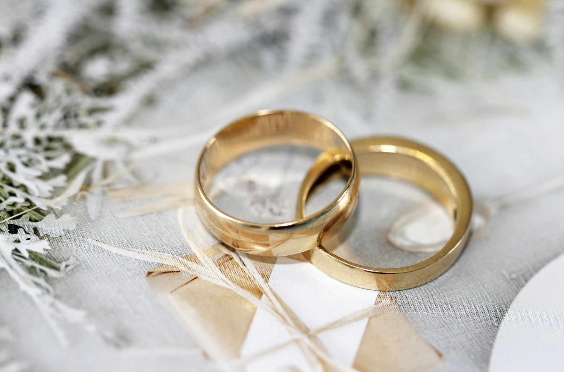 Duas alianças de casamento douradas sobre renda branca com um delicado fundo floral.