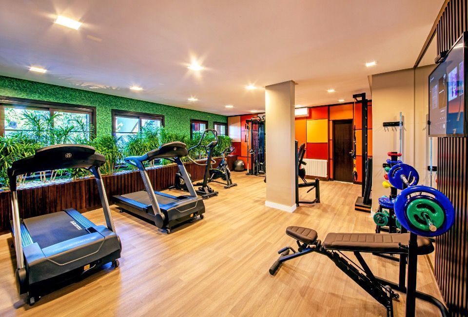 Academia moderna com esteiras, bicicletas ergométricas e aparelhos de musculação em um piso de madeira clara.