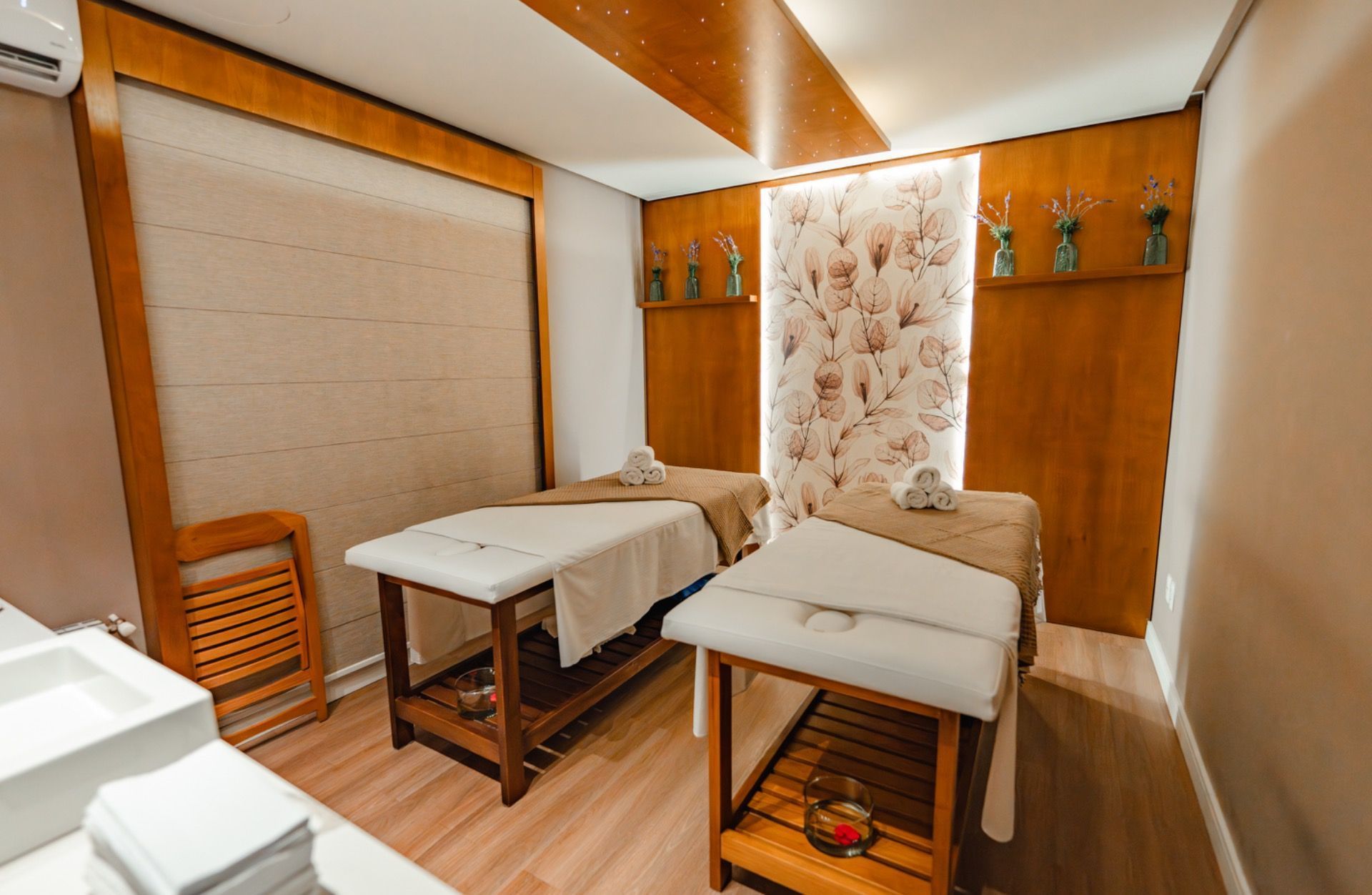 Sala de massagem minimalista com duas macas, paredes bege e armários de madeira.