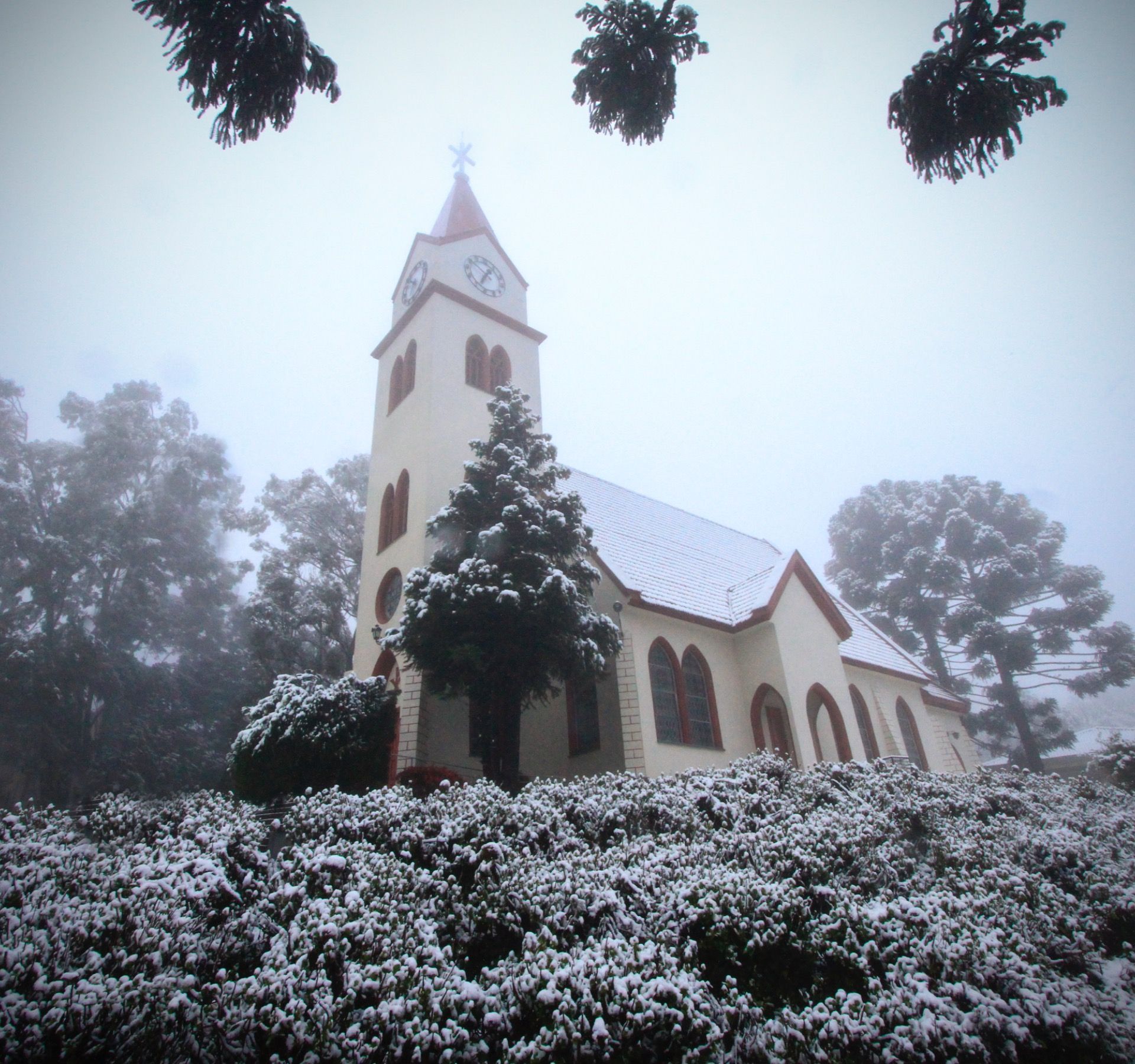 Igreja coberta de neve com uma torre alta em uma paisagem invernal enevoada.