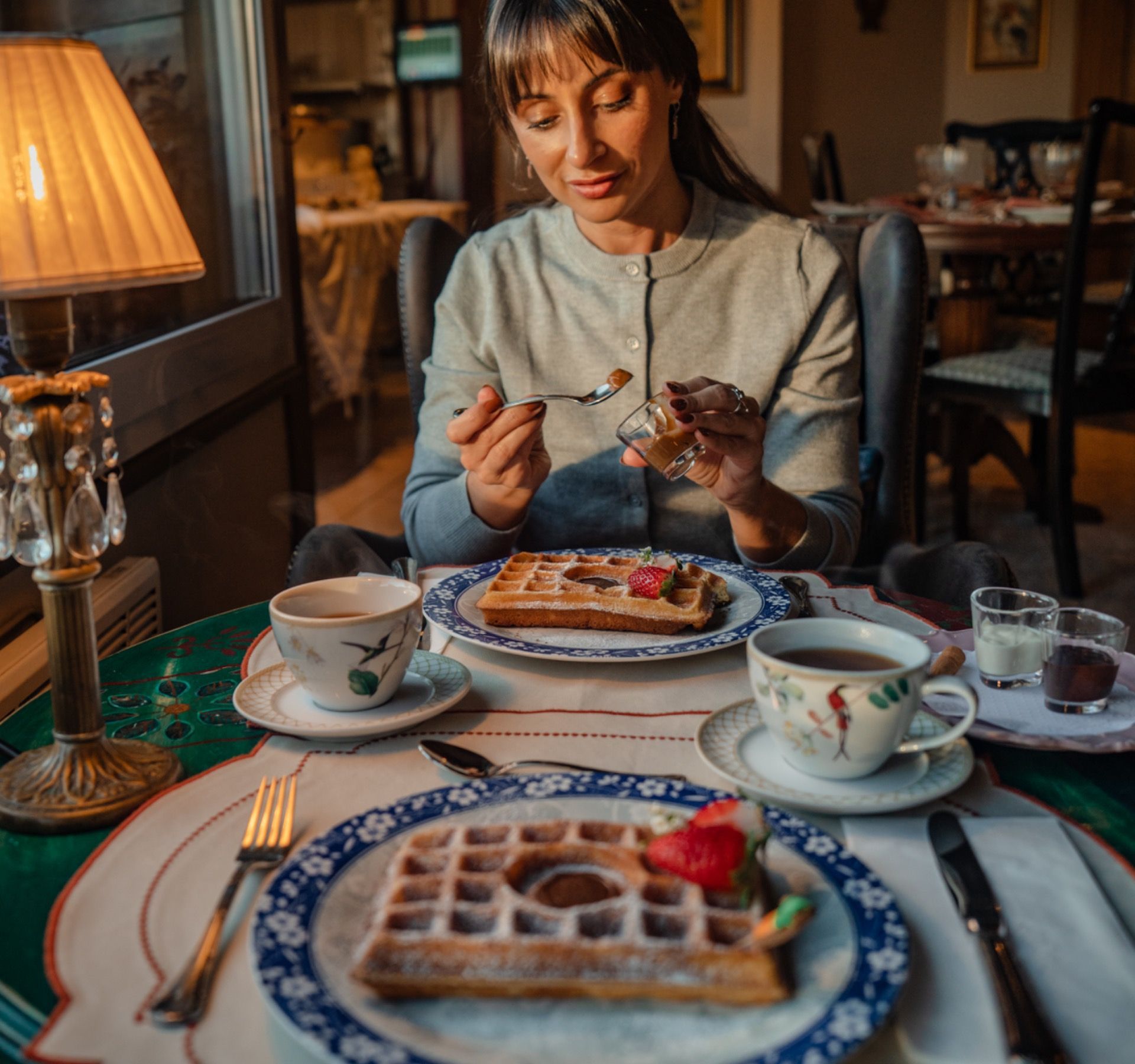 Mulher em um café aconchegante comendo sobremesa à mesa com chá e waffles.