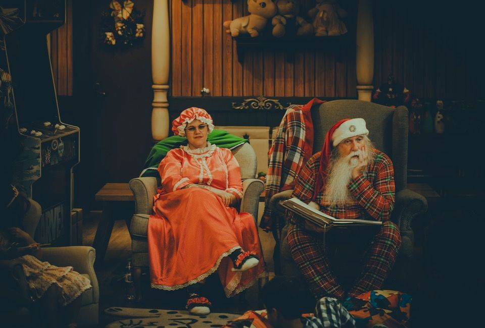 Duas bonecas festivas sentadas em um quarto aconchegante e decorado, uma de laranja e a outra de xadrez com barba branca.