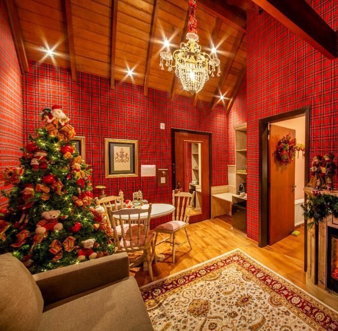 Sala de jantar festiva com paredes vermelhas, árvore de Natal, lustre e mesa posta.