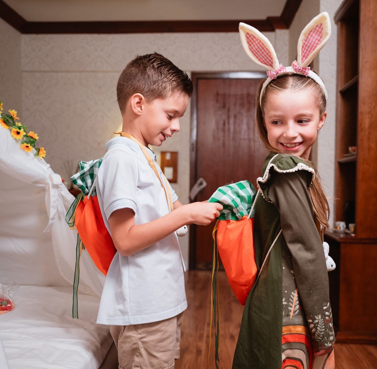 Duas crianças com orelhas de coelho segurando sacolas de doces de Halloween em um corredor.