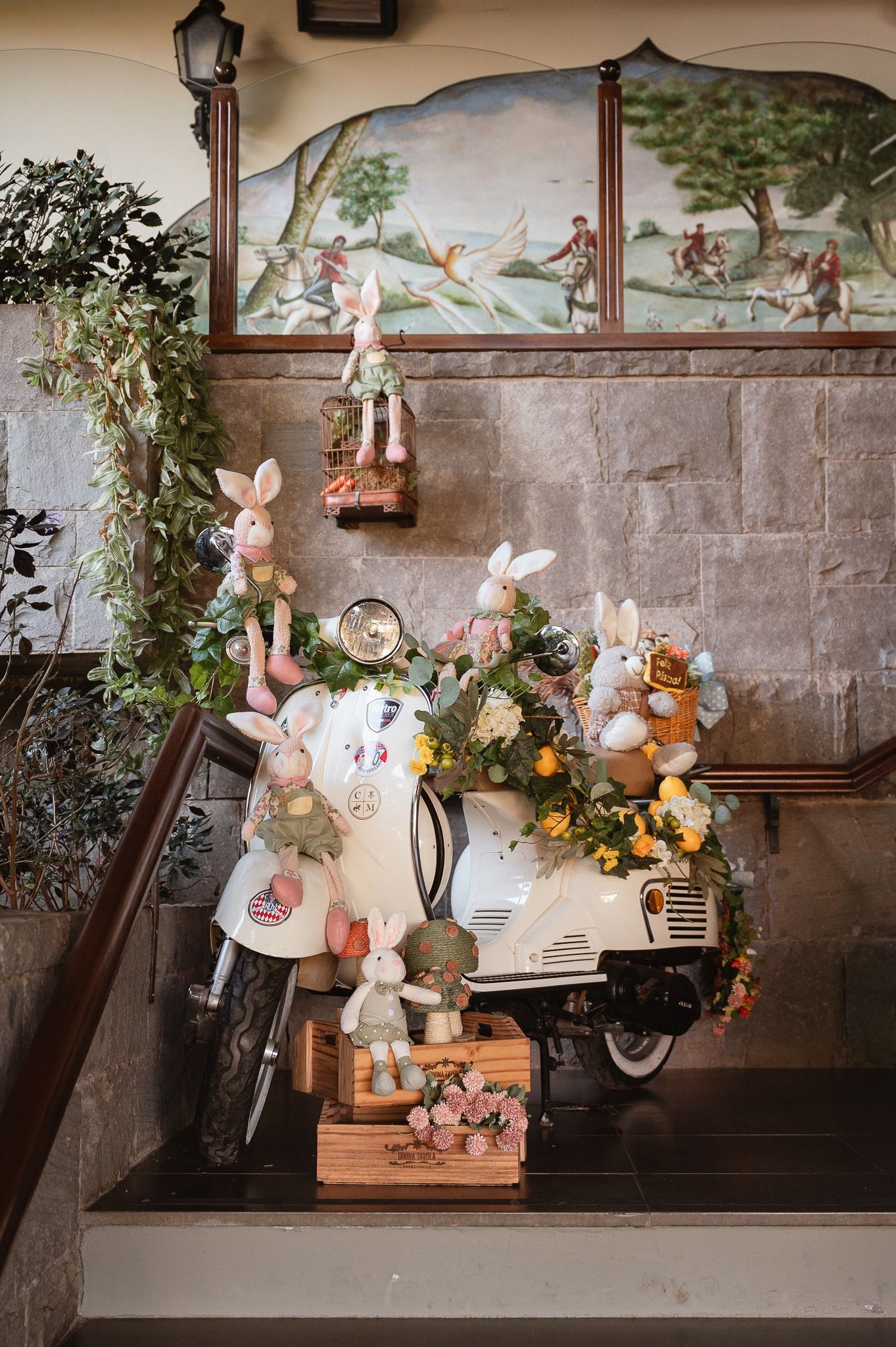 Altar funerário decorativo branco com flores, animais empalhados e lanternas contra uma parede de pedra.