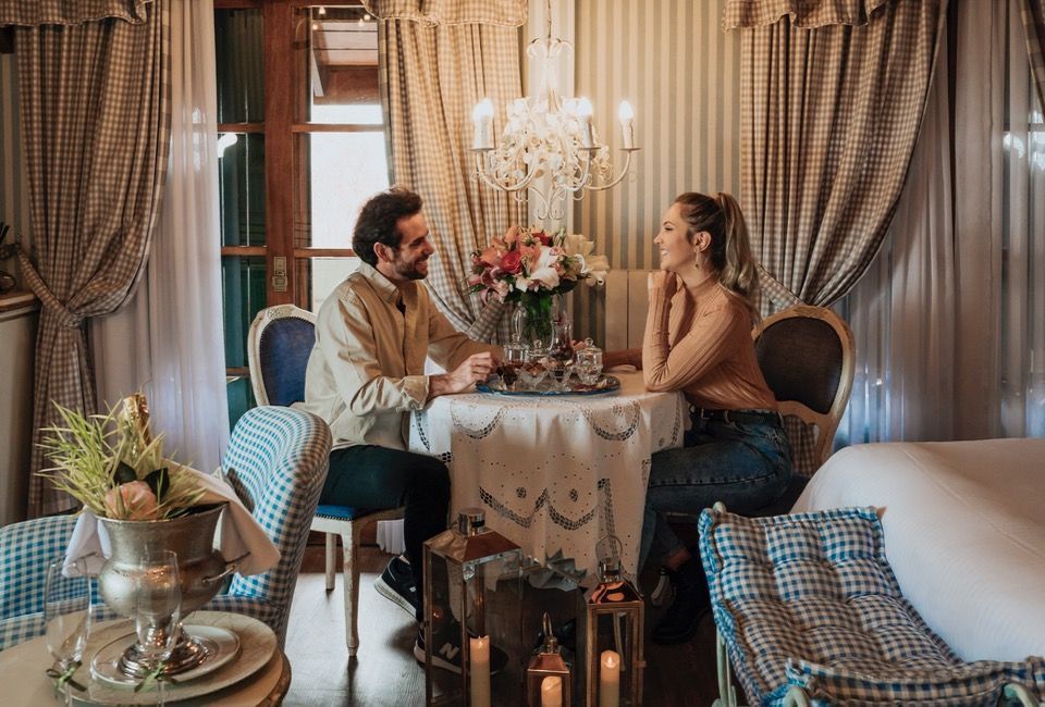 Casal conversando à luz de velas em um aconchegante salão de restaurante com cortinas.