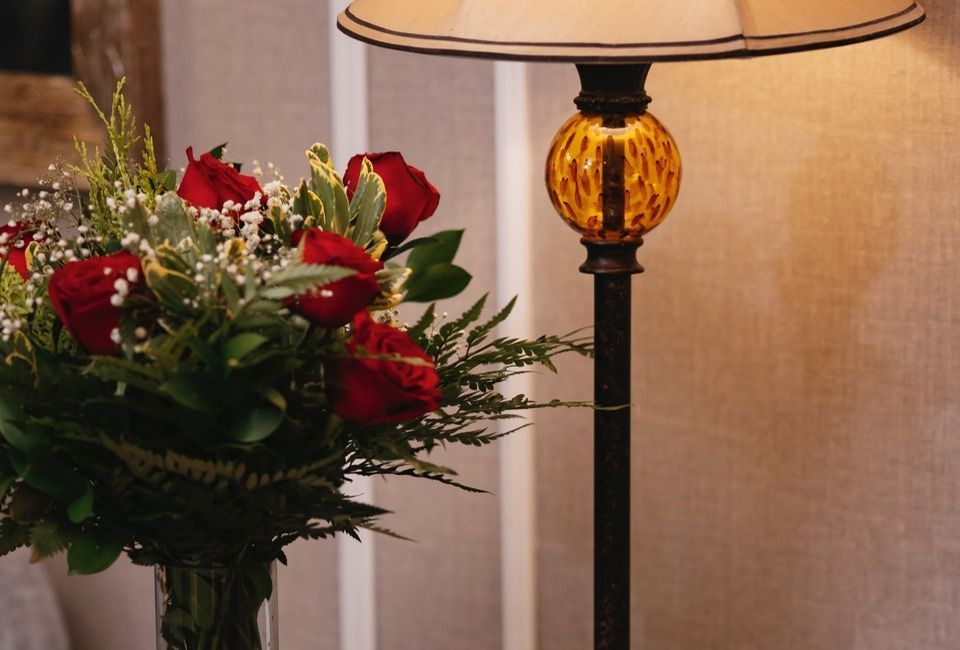 Rosas vermelhas num vaso ao lado de um candeeiro de mesa aceso num ambiente interior acolhedor.