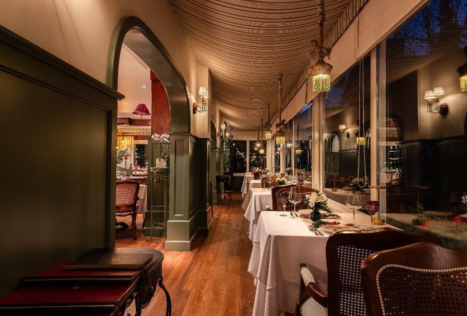 Sala de jantar elegante de restaurante com toalhas de mesa brancas, iluminação aconchegante e janelas em arco ao longo da parede.