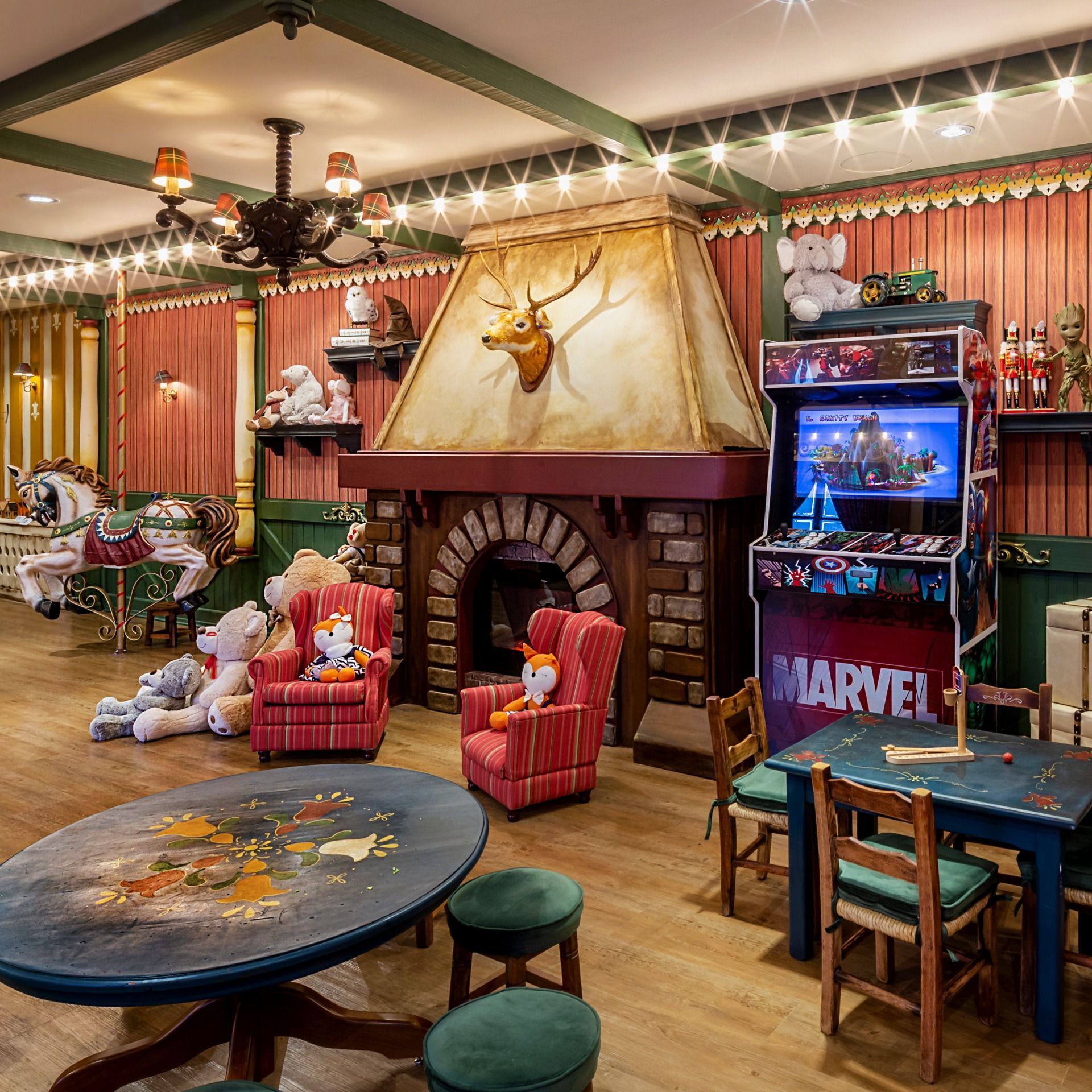 Quarto temático aconchegante com lareira de pedra, decoração com chifres, cadeiras coloridas e máquinas de fliperama da Marvel.