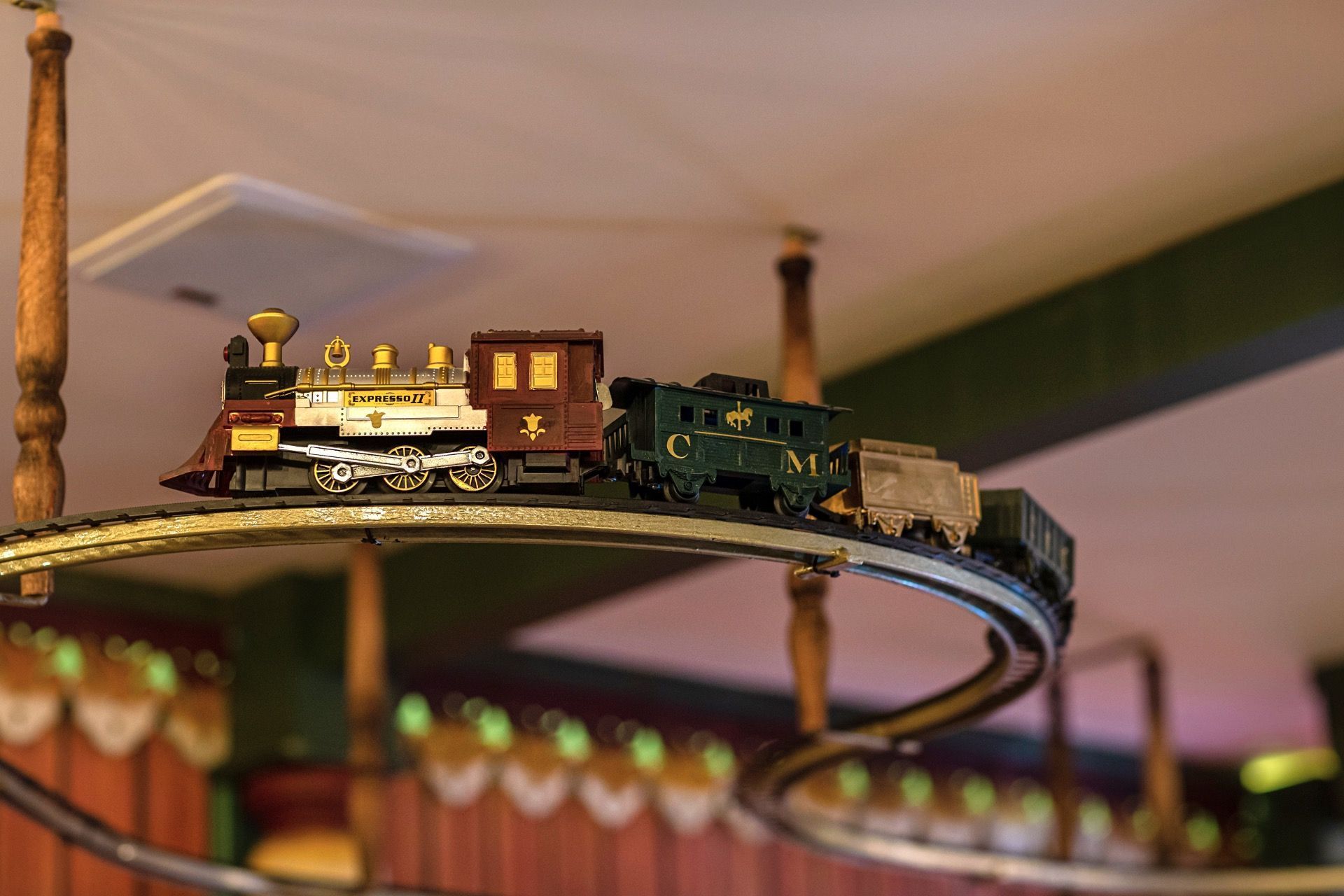 Trem de brinquedo em miniatura circulando em um trilho circular em ambiente interno, com uma pequena locomotiva e vagões.
