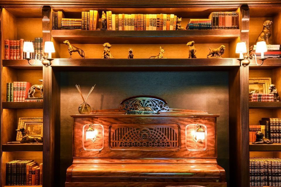 Biblioteca com iluminação aconchegante, estantes de madeira, piano e lareira.