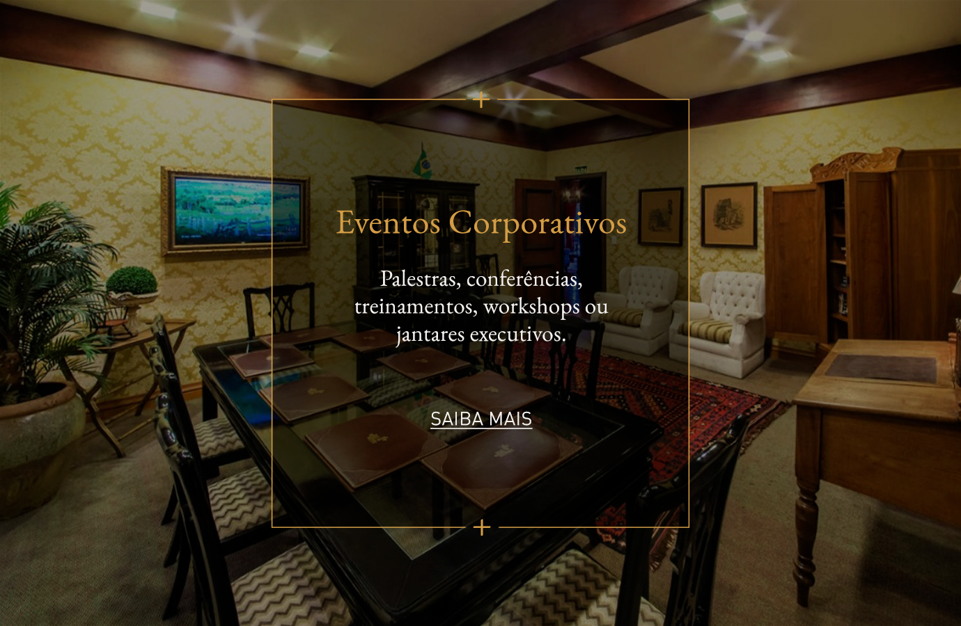 Interior de um espaço para eventos com mesa de conferência, cadeiras de couro e painel com a inscrição “Eventos Corporativos”.