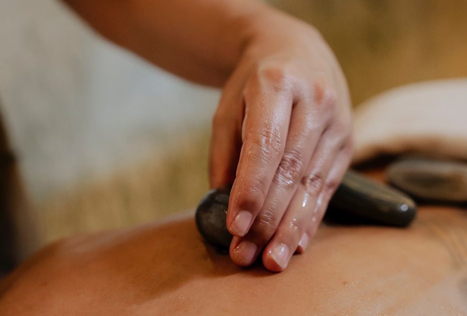 Mão colocando pedras quentes nas costas nuas de uma pessoa durante uma massagem.