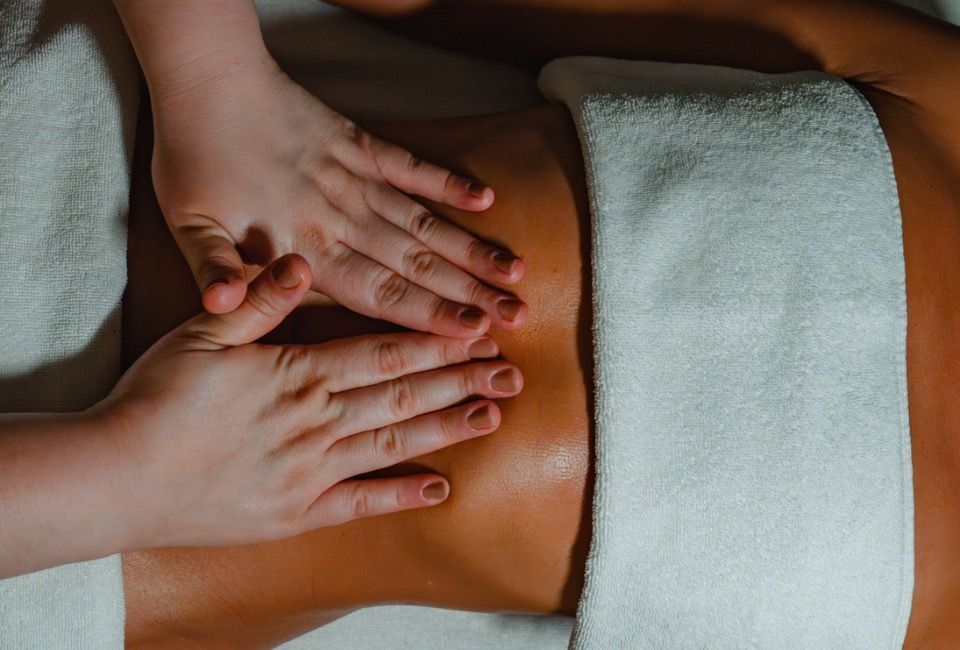 Mãos massageando as costas com toalhas brancas em um ambiente de spa.