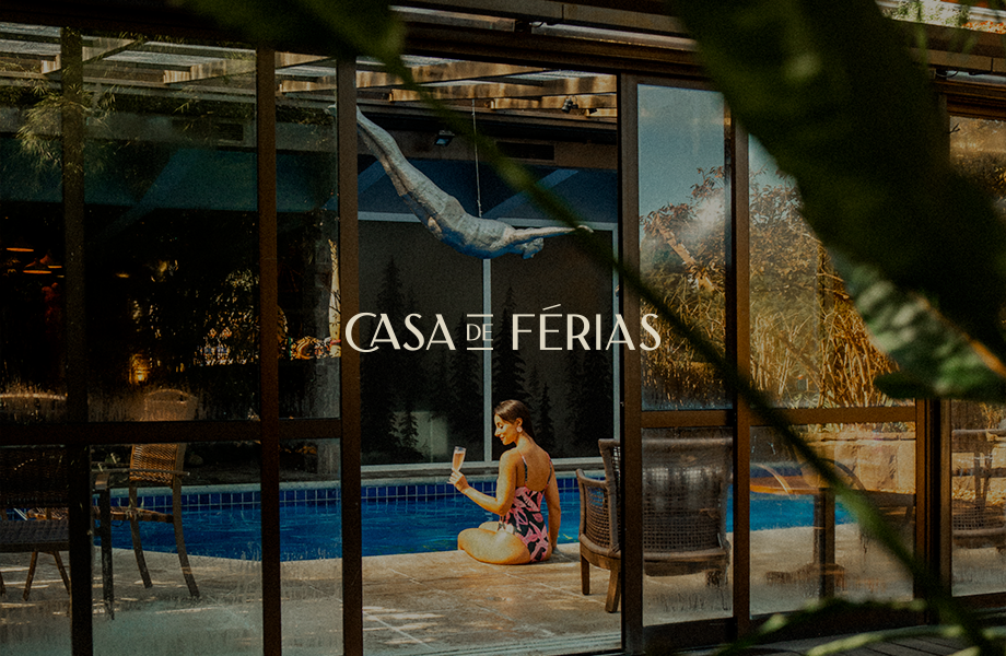Casa de férias com uma pessoa sentada junto a uma piscina azul atrás de portas de vidro.