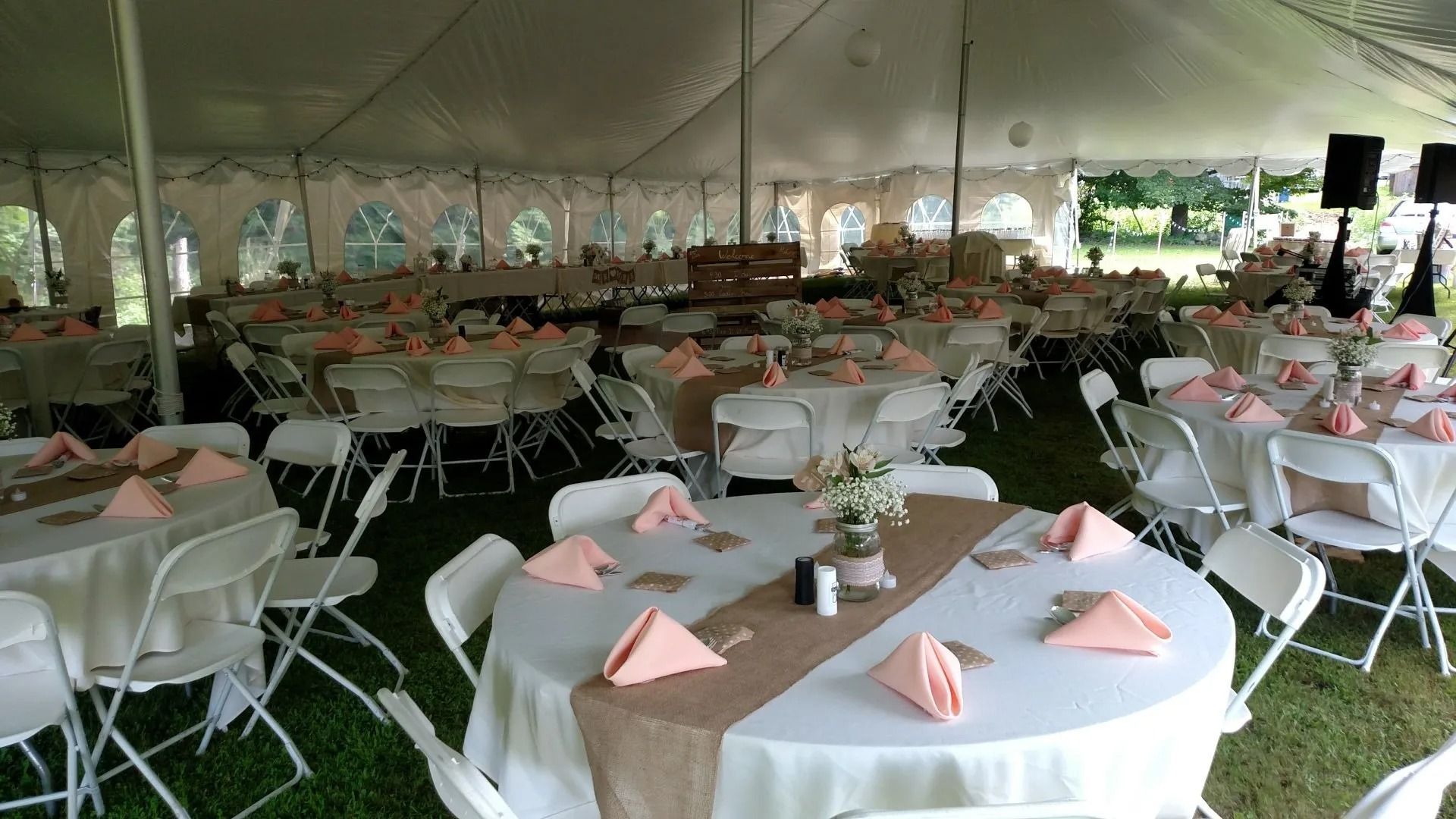 Banquet tent with round tables, white chairs, and pink folded napkins set for an event