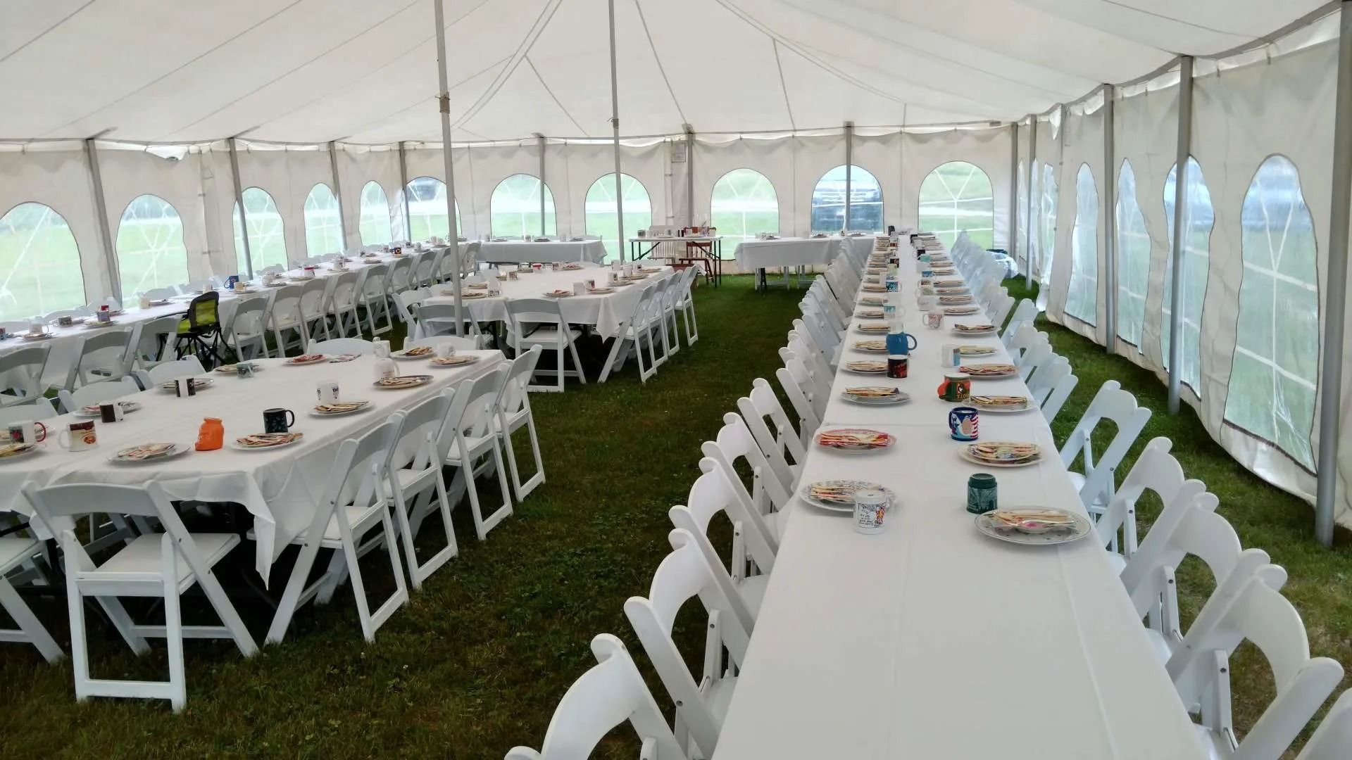 Large white event tent with long banquet tables, white chairs, and place settings on grass