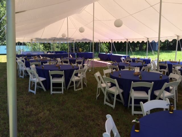 White tent with round tables and white chairs set up for an outdoor event on grass