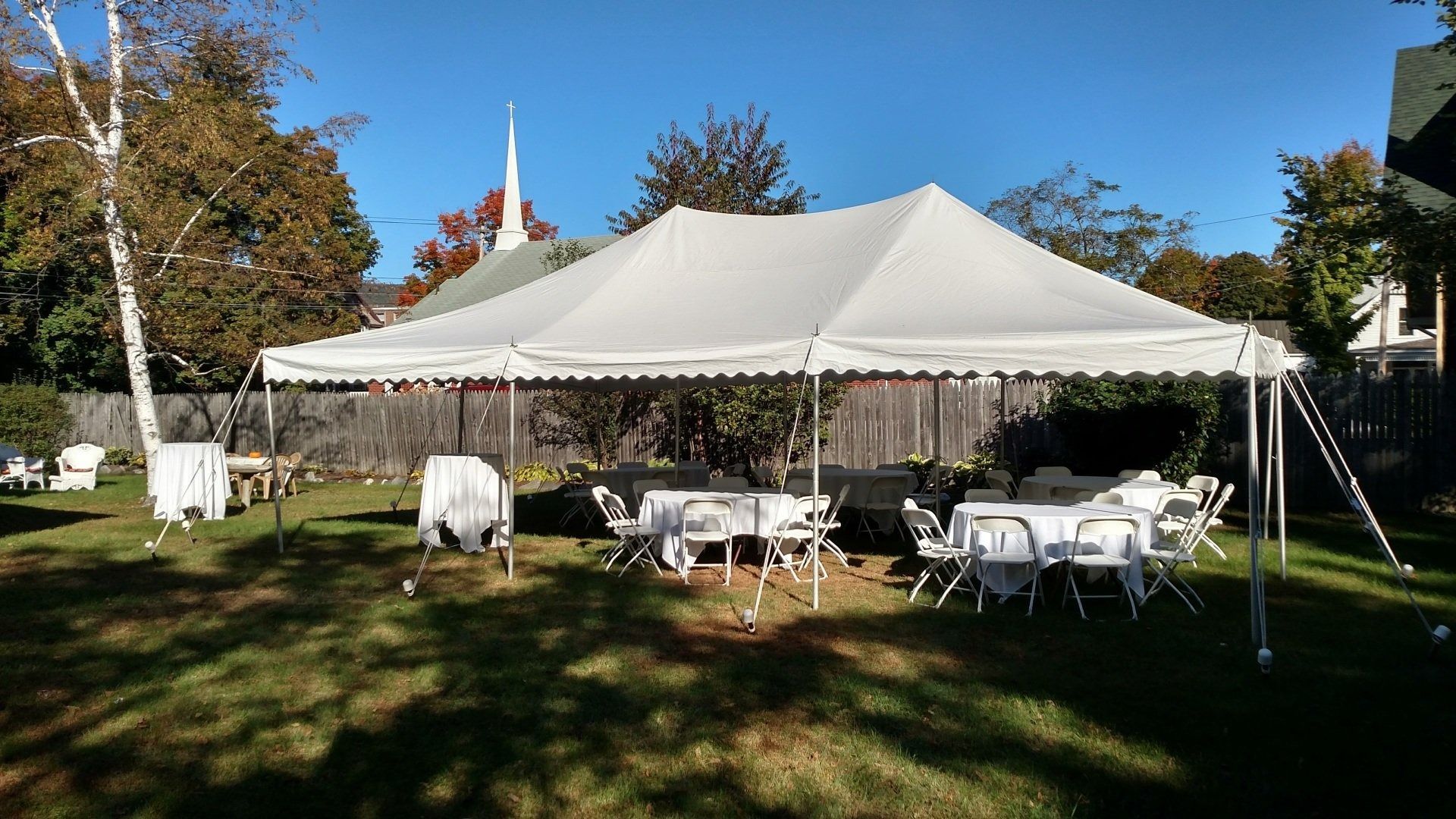 White event tent with tables and chairs set up on a grassy lawn outdoors