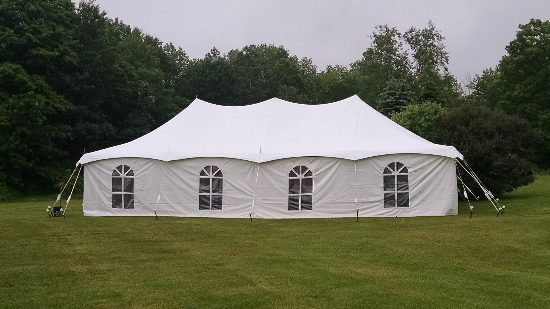 Large white event tent on a grassy field surrounded by trees