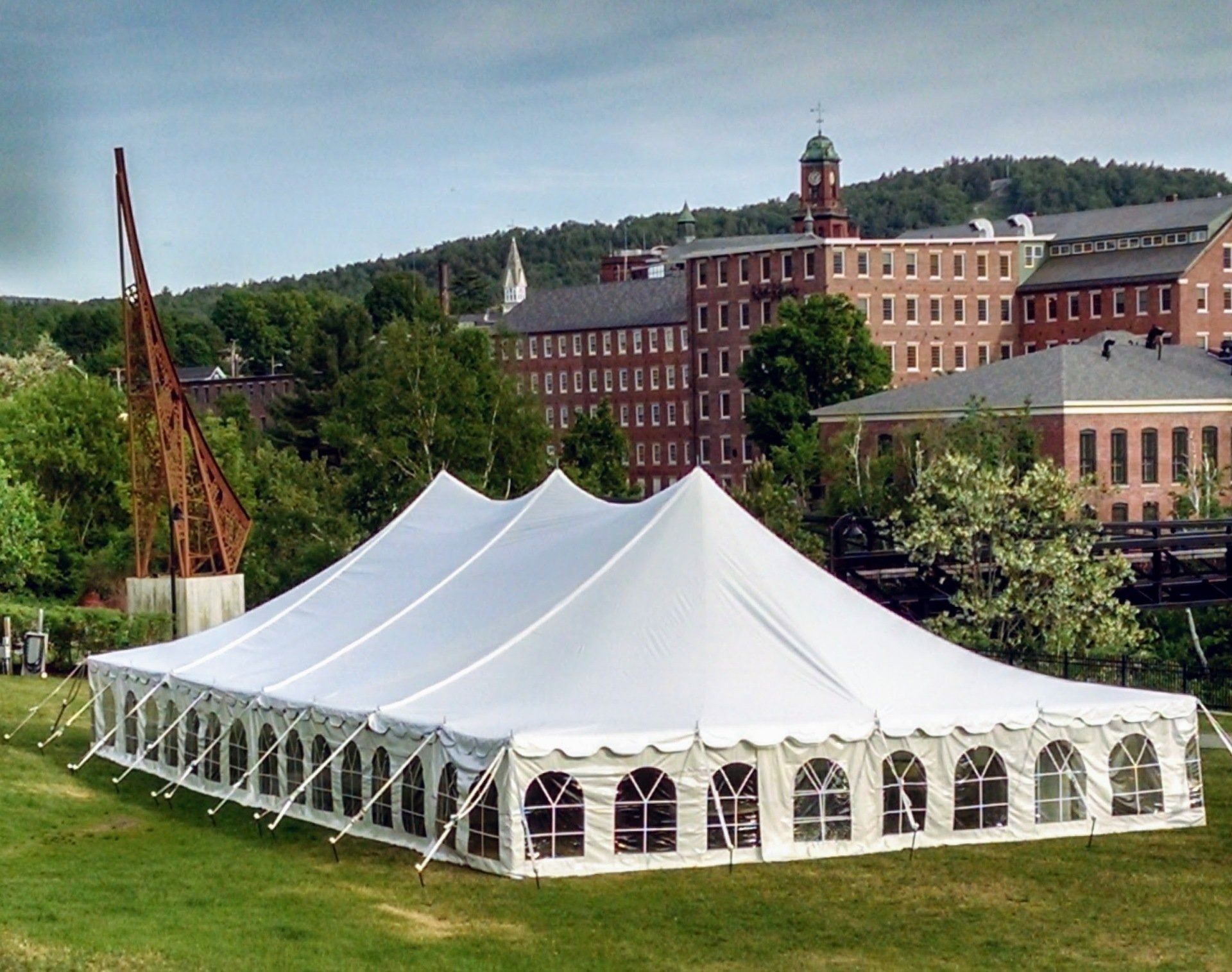 Large white event tent on a grassy lawn near a brick building and trees