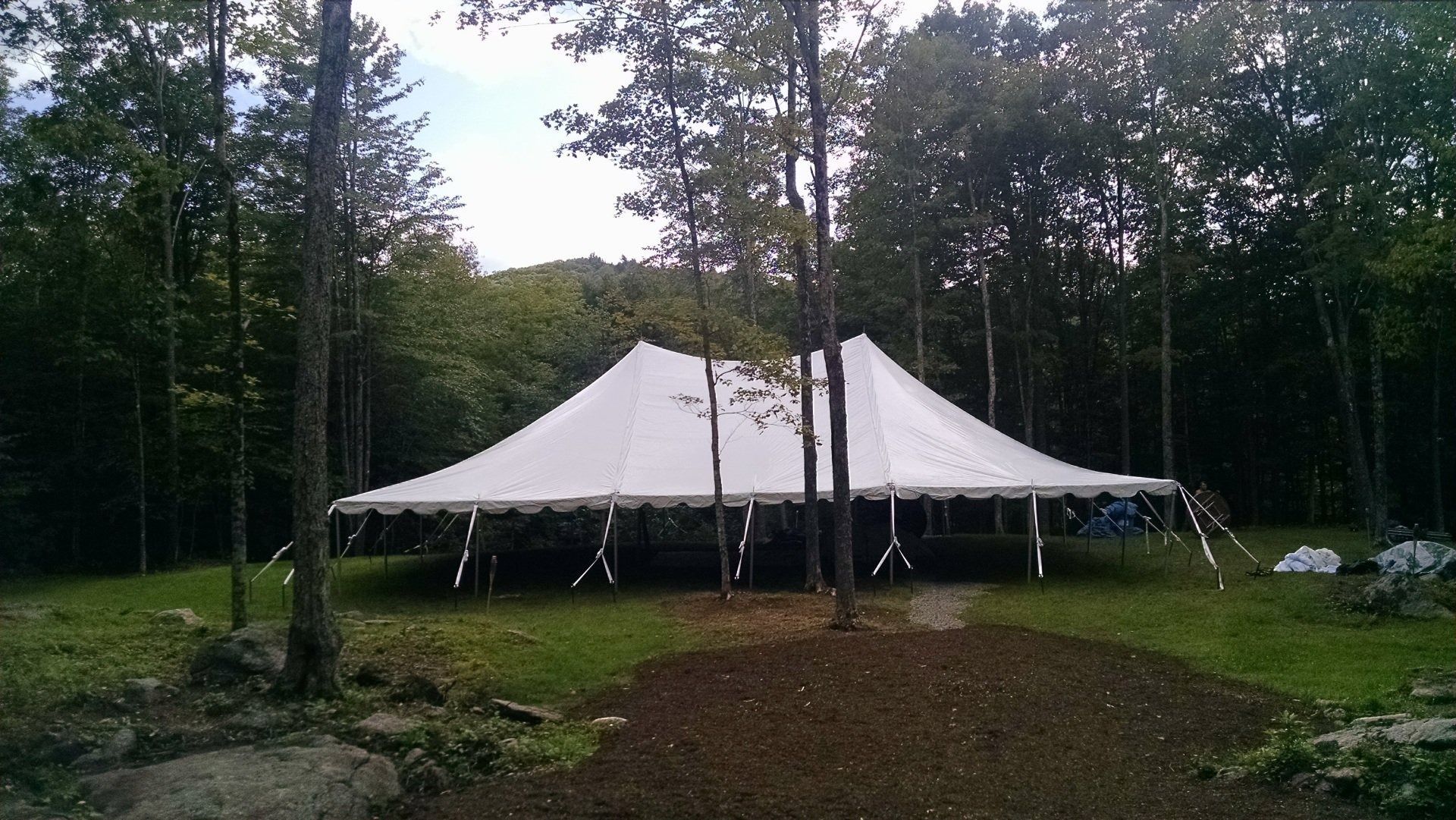White event tent in a wooded clearing at dusk