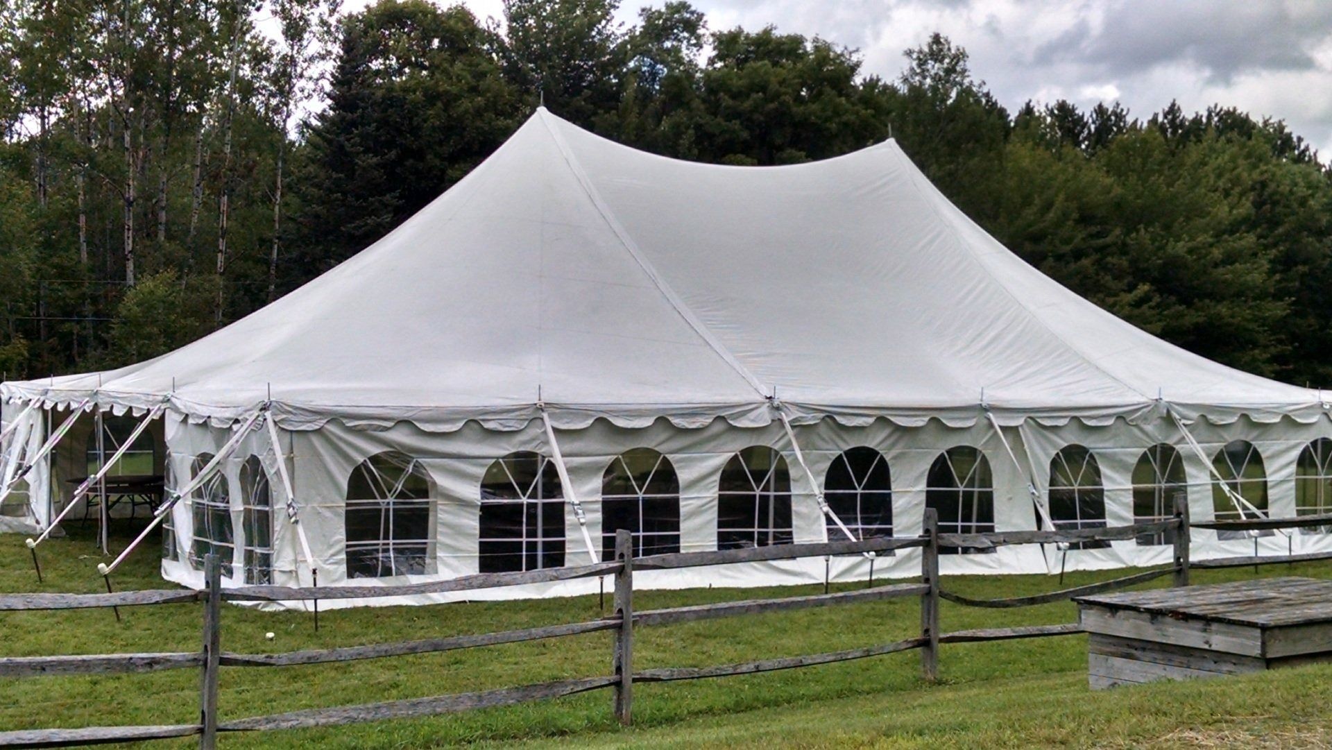 Large white event tent on a grassy field with trees and a wooden fence nearby
