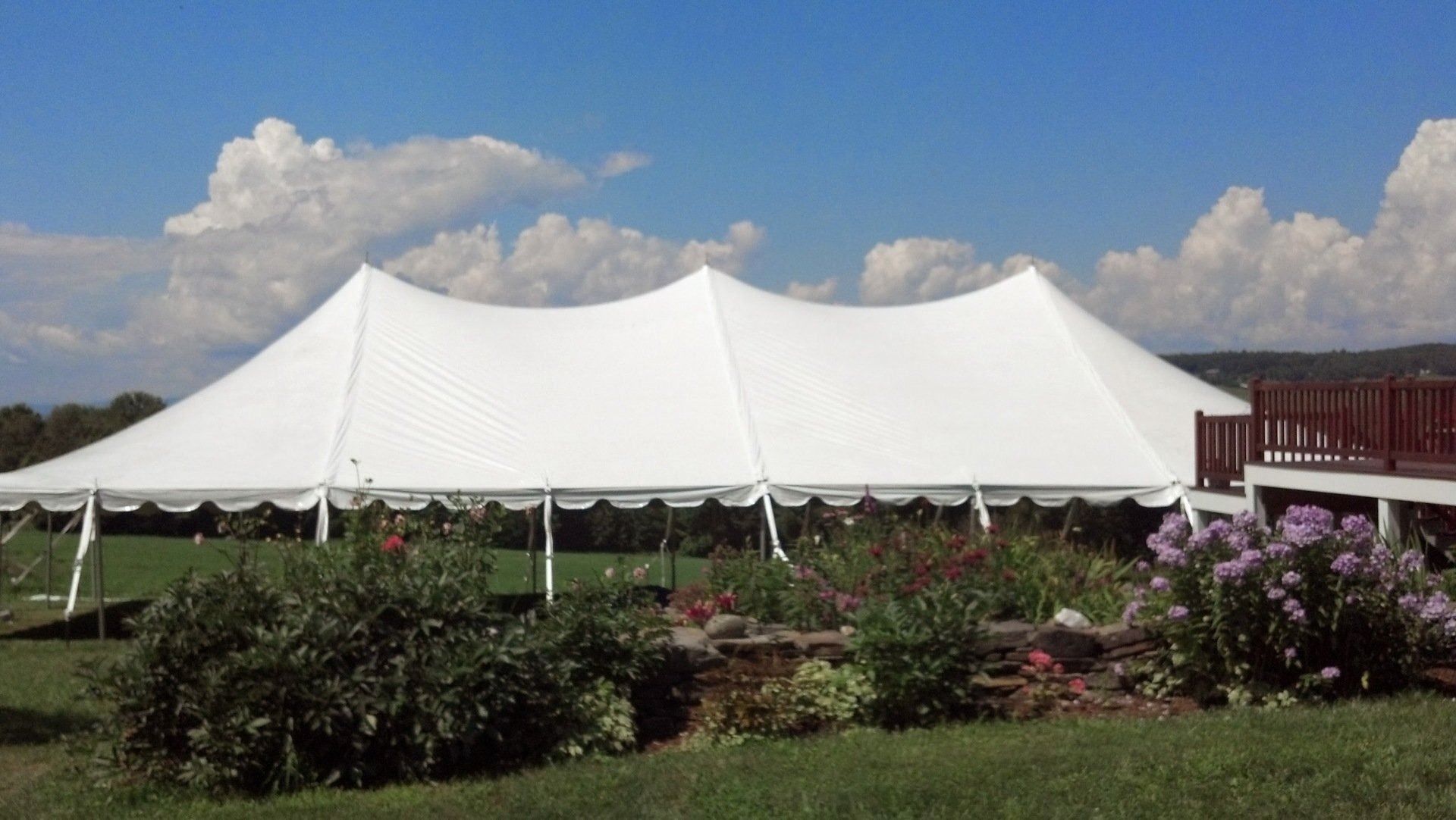 Large white event tent in a garden under a blue sky with clouds