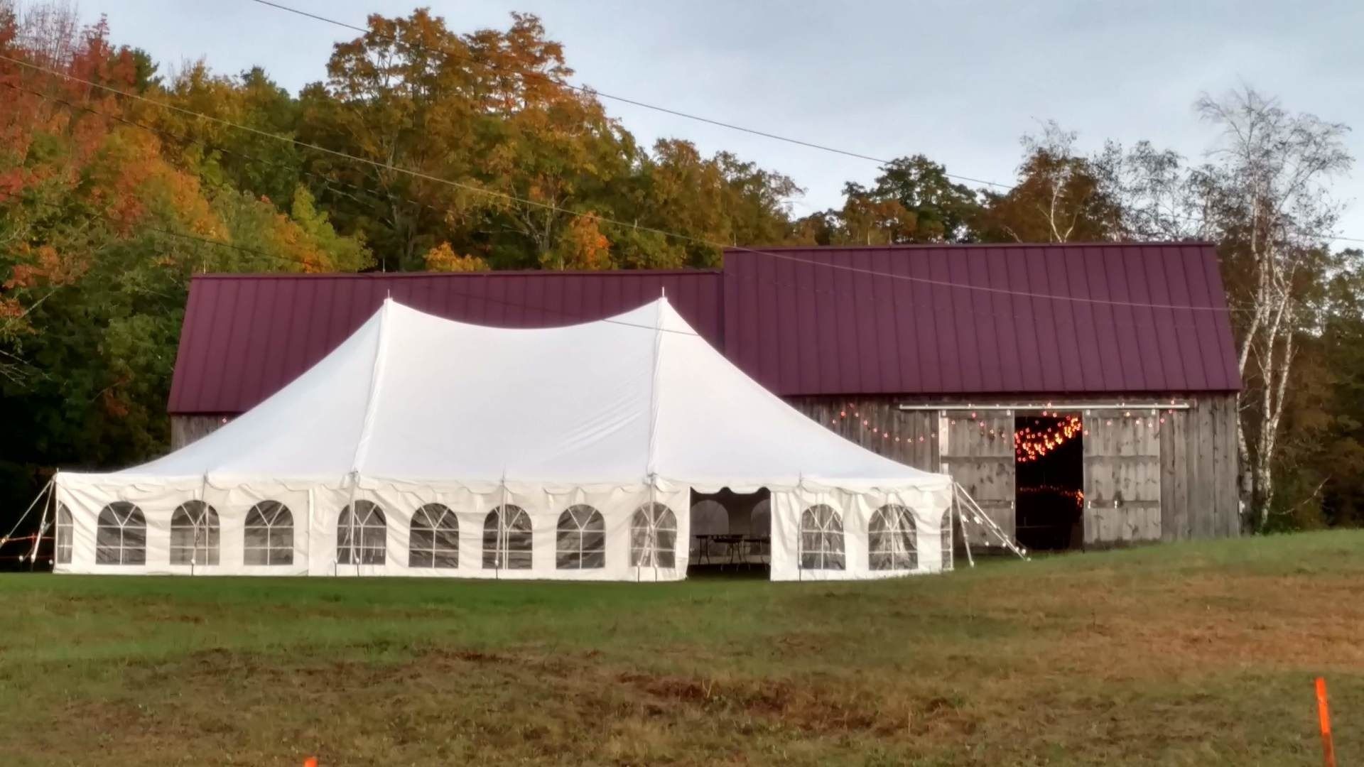 White event tent beside a rustic barn with a red roof in a grassy field