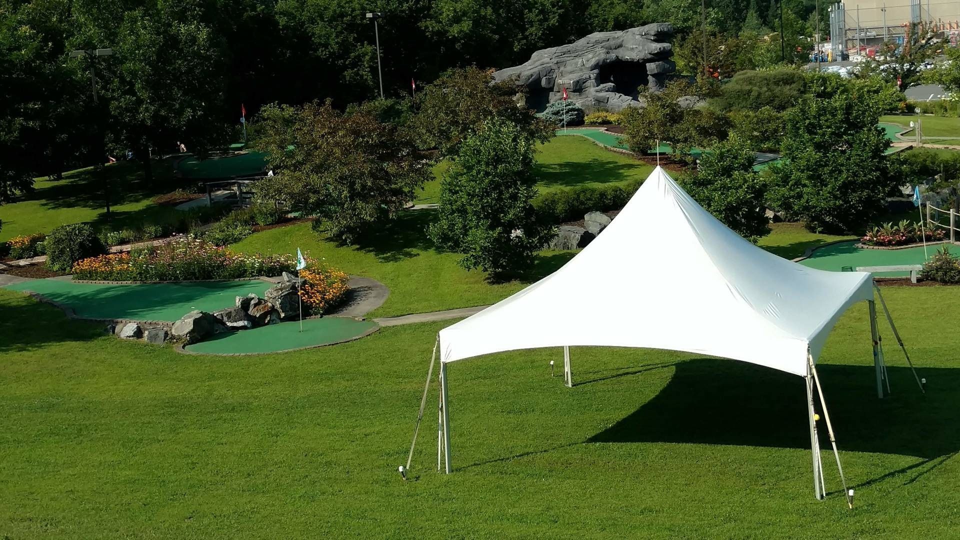 White canopy tent on a green lawn in a park with trees and rocks in the background